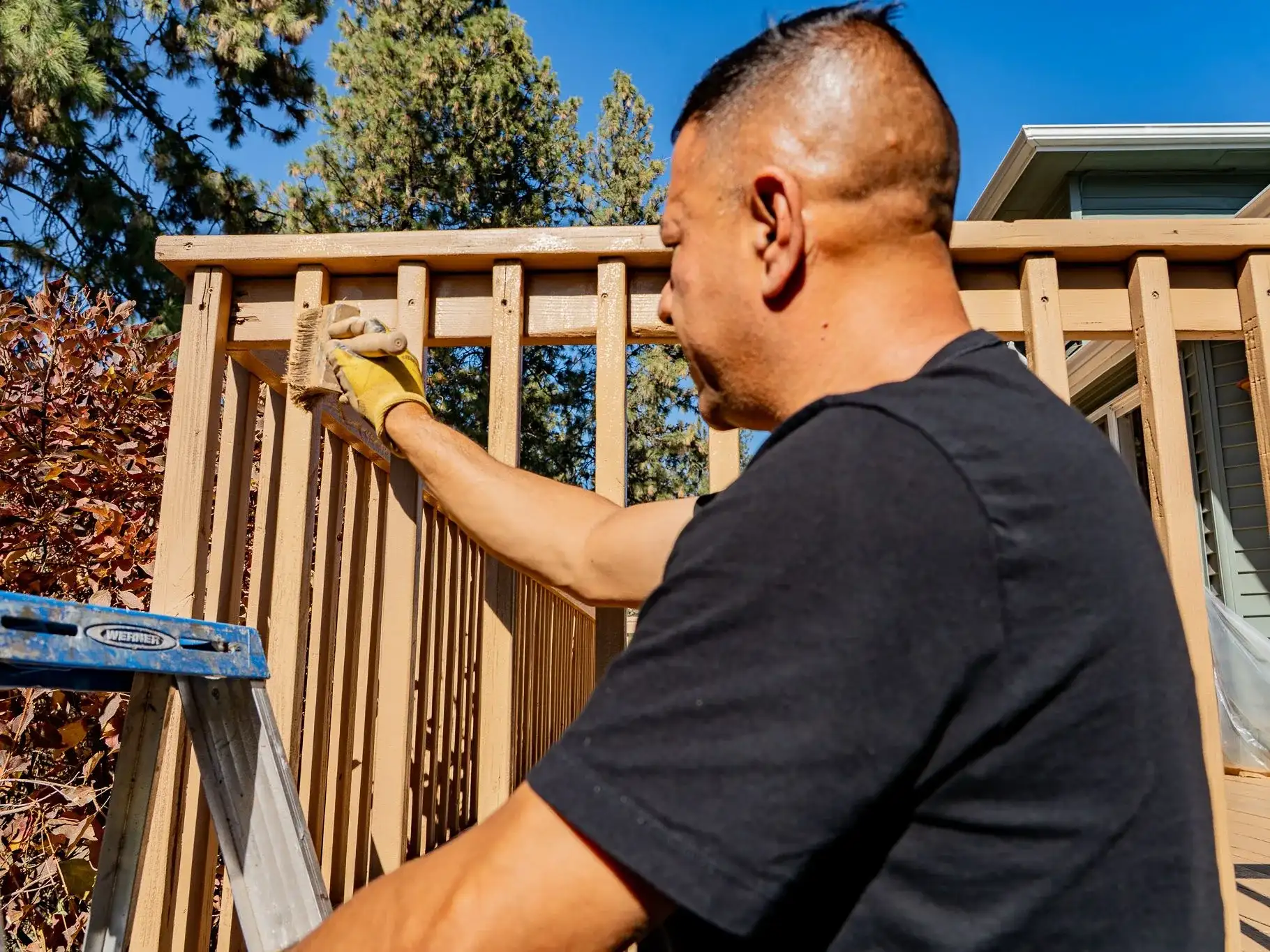 Casa Vida painter in work gloves brushing stain along the top rail of a deck