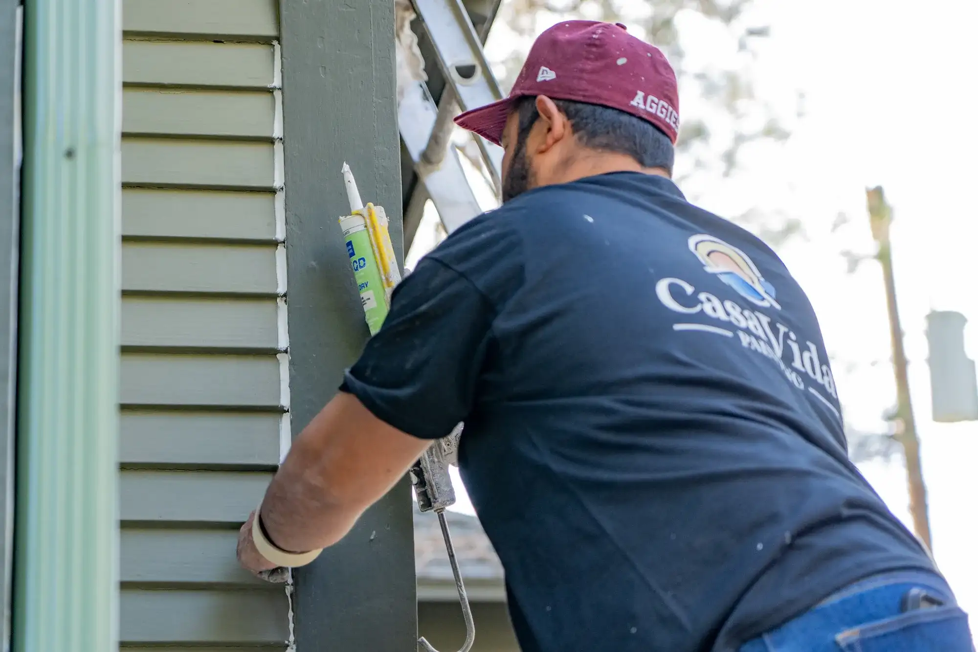 Casa Vida painter caulking the joint between green siding and trim