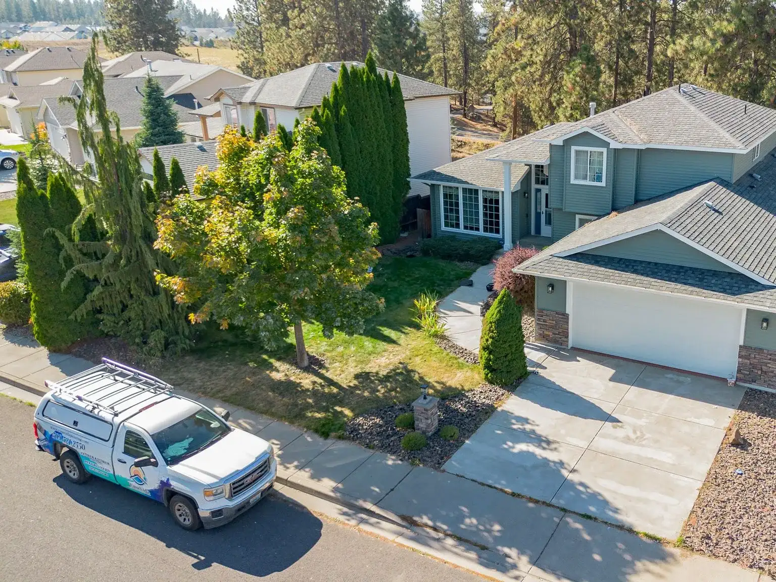Drone view of the Casa Vida truck parked at the curb in front of a sage-green two-story home with white trim