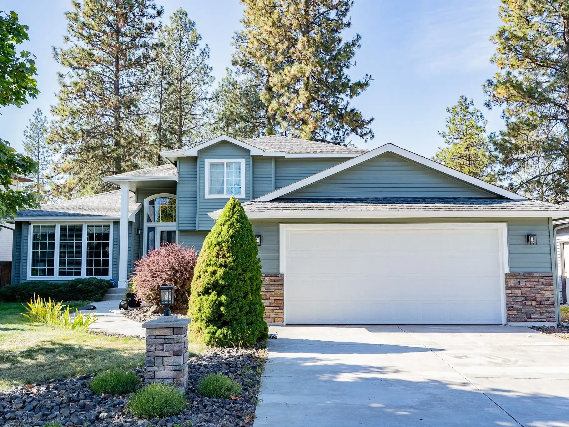 Front of a sage-green two-story home with fresh white trim, a white garage door and stone columns