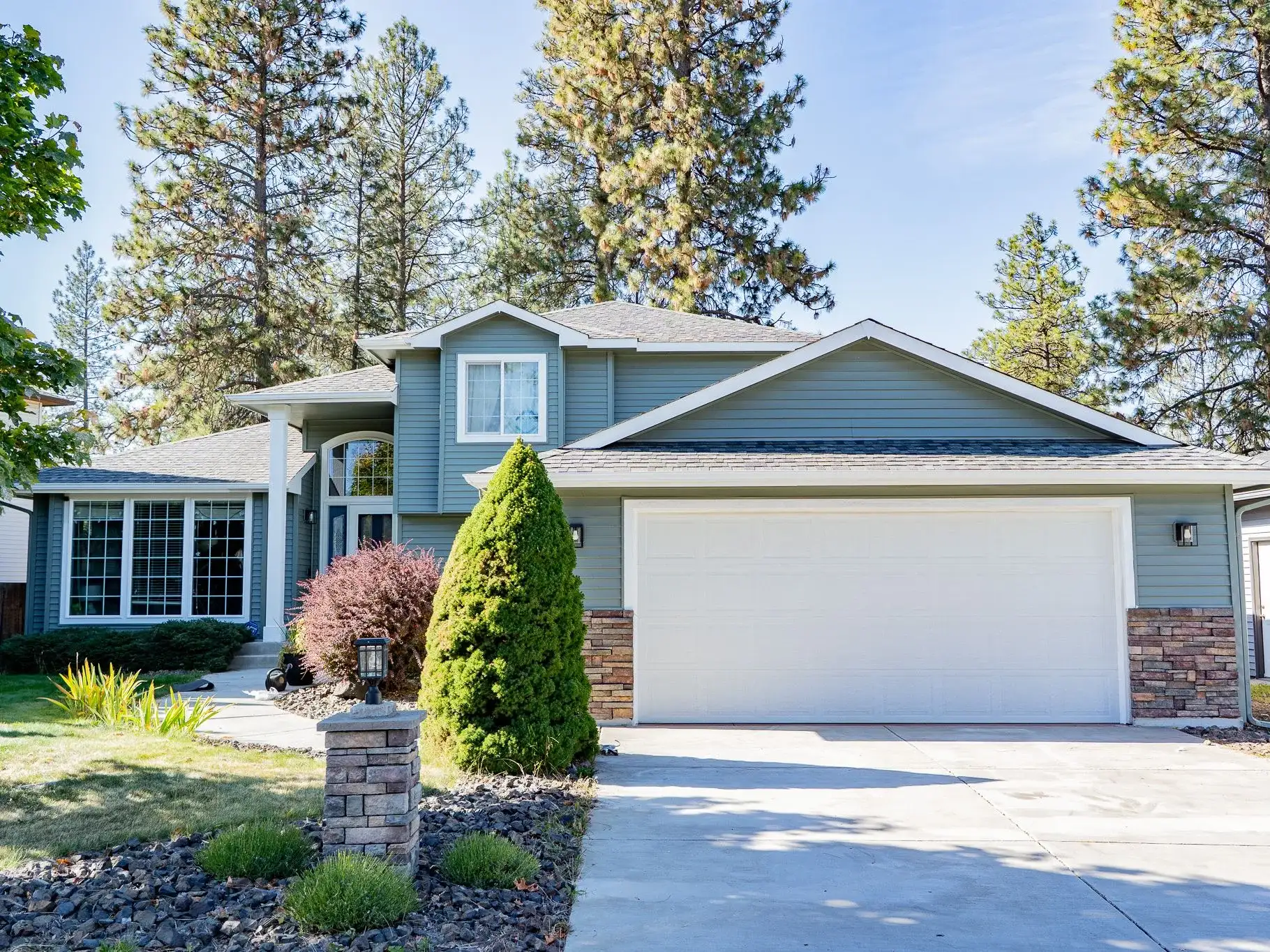 Front of a sage-green two-story home with fresh white trim, a white garage door and stone columns