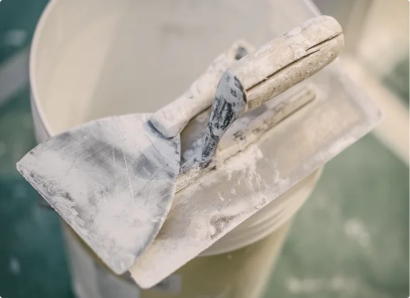 Plastering tools covered in white compound resting on the edge of a bucket