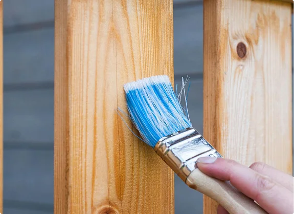 Close-up of hand painting a wooden fence with a brush
