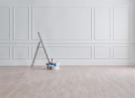 Minimalist room with white paneled wall, wooden floor, ladder, and painting supplies
